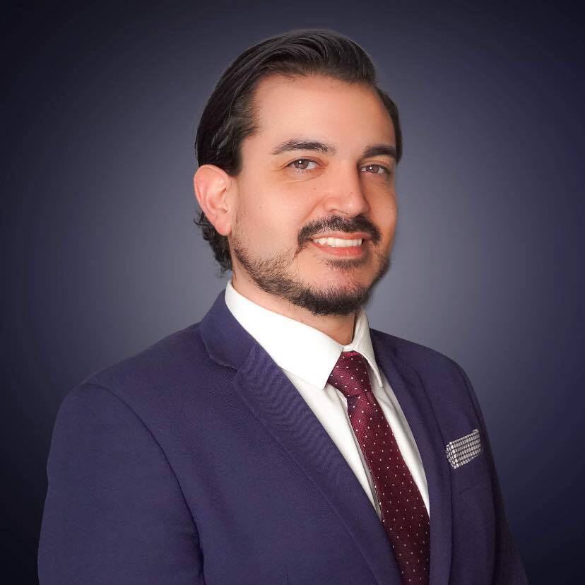 Professional headshot of Les Lopez in formal business attire, smiling confidently against a neutral background